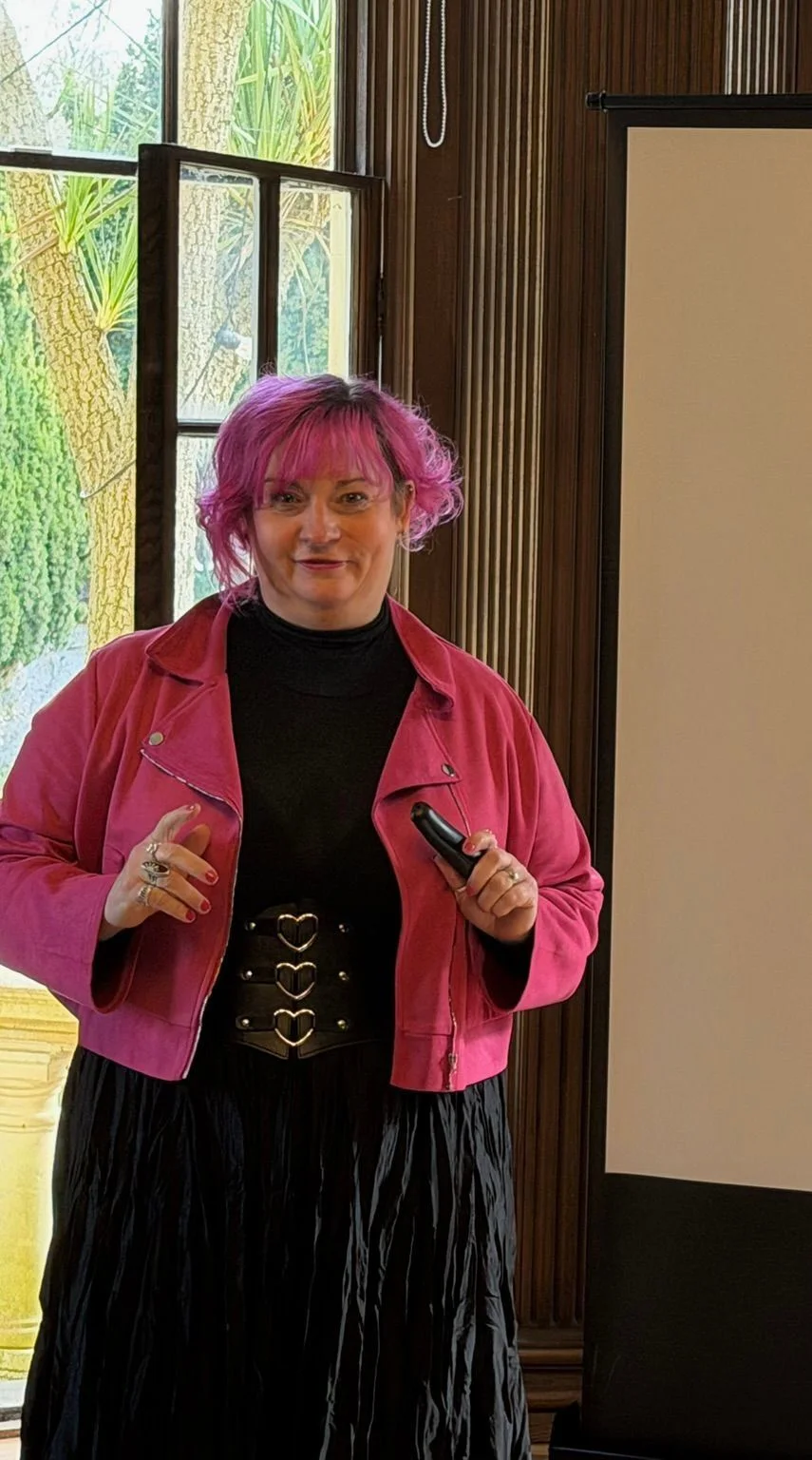 Belinda Warburton standing beside a presentation screen in a wood-panelled room.