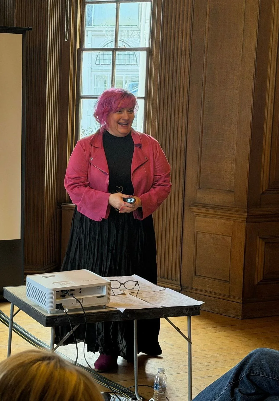 Belinda Warburton speaking in a wood-panelled room with an audience.